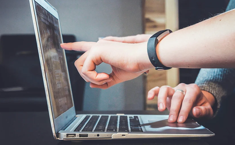 A photo of multiple people working at a laptop, pointing at details on the screen.