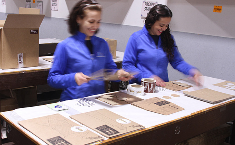 A photo of two fulfillment employees working at the packing station.